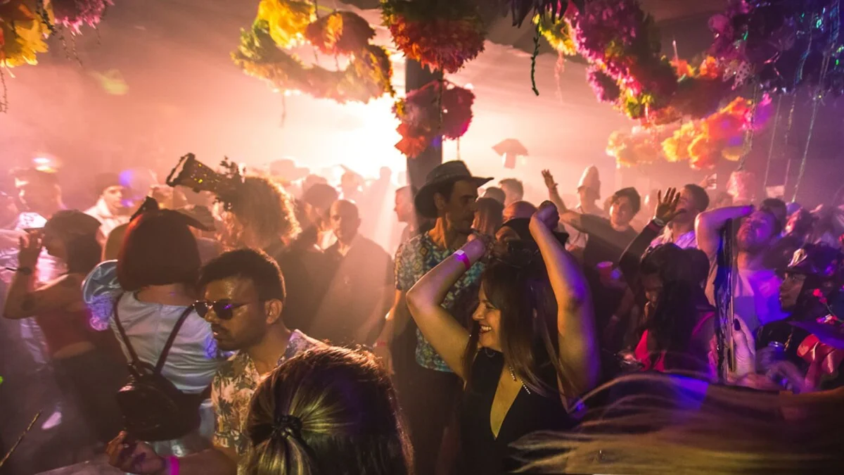 A crowd of people dancing with a yellow glow behind them from a flash