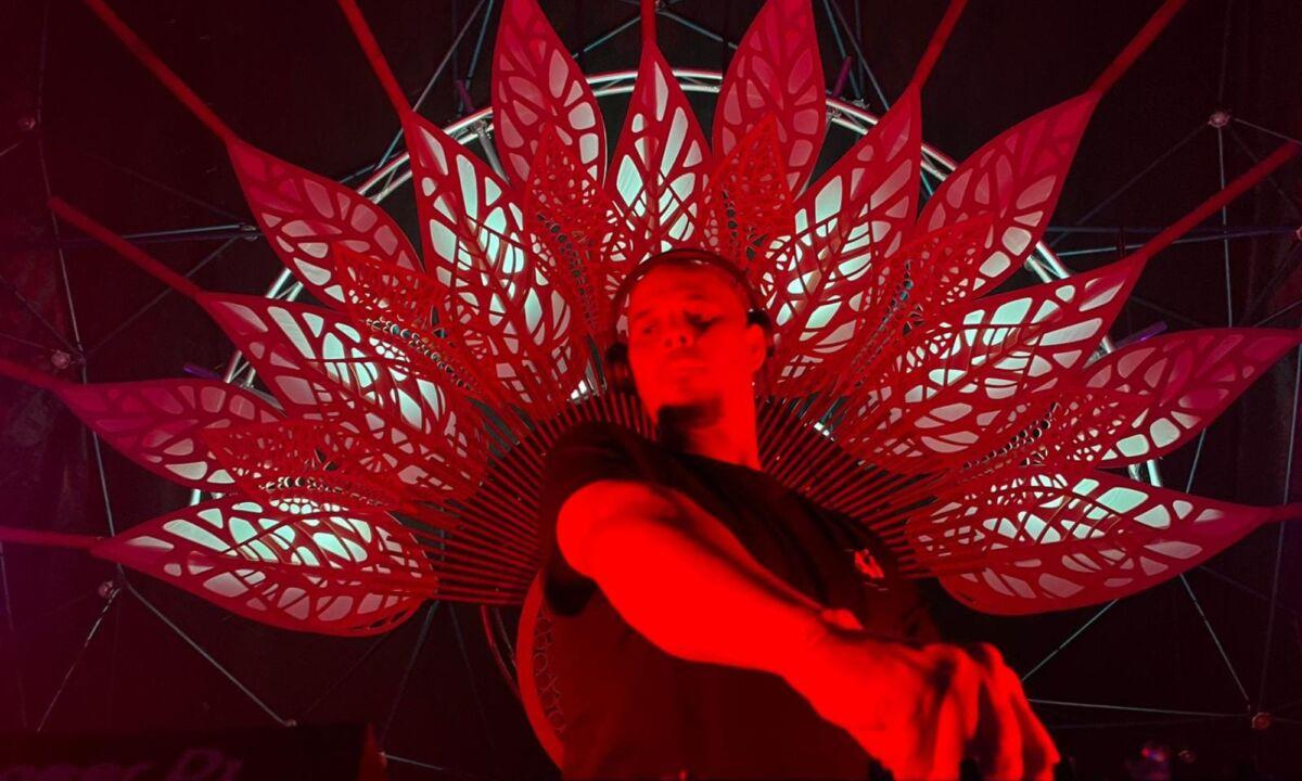 Red lit man with arm reaching towards a knob. A red lit fan of wood leaves is behind him.