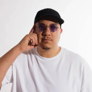 A man with black cap wearing a white T. He has a finger to his ear