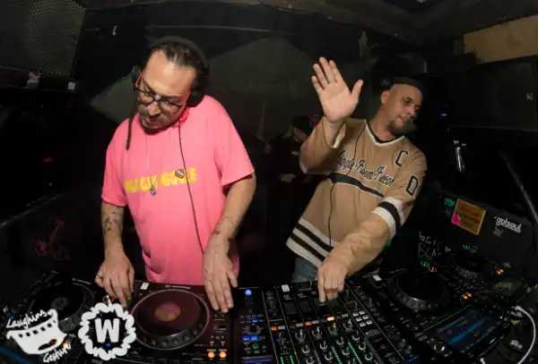Two DJs, one with hand up