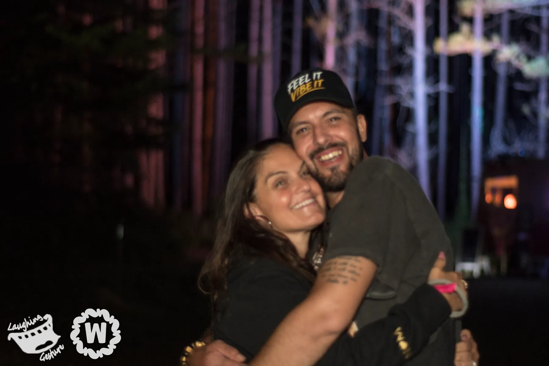 Couple hugging at Camp Wiggly festival, man wears "Feel It Vibe It" hat.