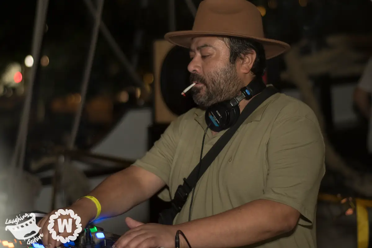 DJ in a hat and headphones plays music at an event, smoking a cigarette.