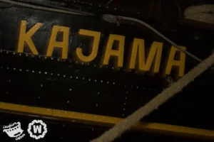 The name KAJAMA is painted in yellow on the dark hull of a ship.