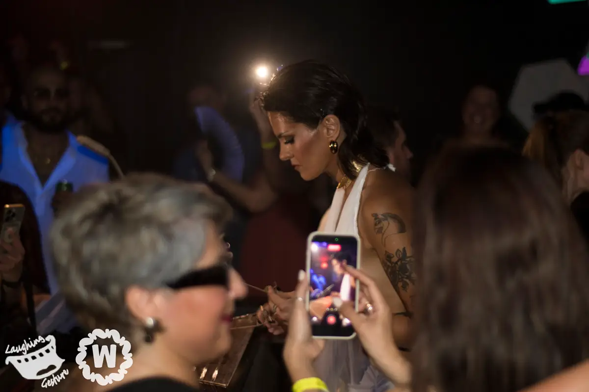 Woman in white dress takes photo of performer with phone at event
